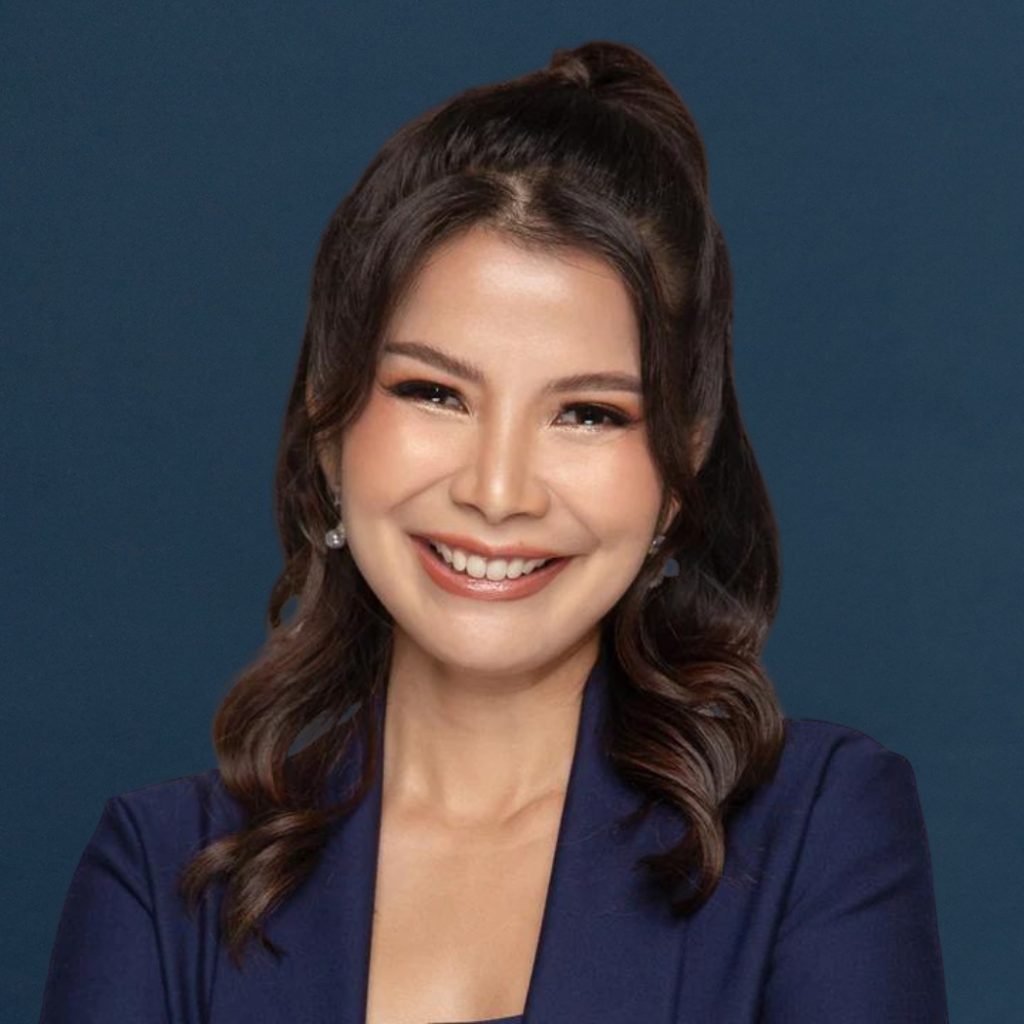 Portrait of a smiling team member with wavy dark hair tied half-up, wearing a navy blazer against a dark blue background.