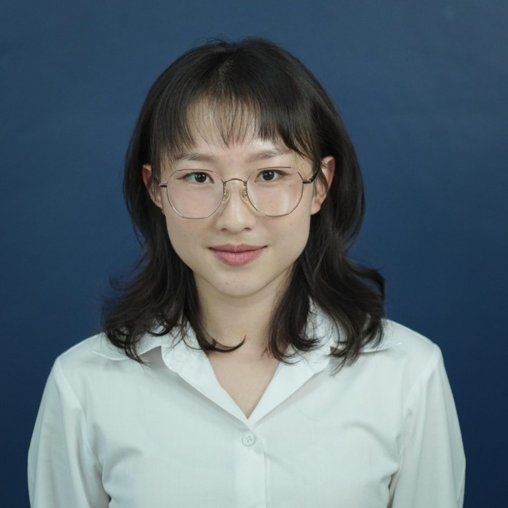 Portrait of a team member wearing glasses and a white shirt, with shoulder-length dark hair, standing against a dark blue background.