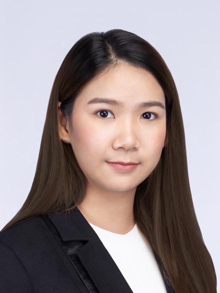 Portrait of a team member with long dark hair, wearing a black blazer and white top, against a light background.